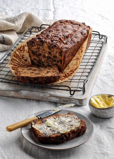 Image of Bara Brith on baking rack with slice on plate covered in salted butter 